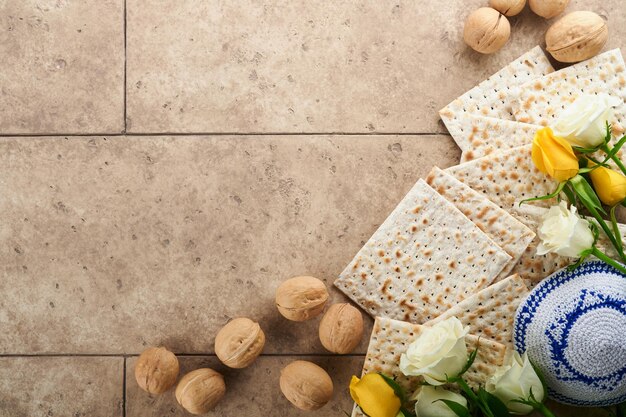 Passover celebration concept Matzah kosher red wine walnut and white and yellow roses Traditional ritual Jewish bread on sand color old tile wall background Passover food Pesach Jewish holiday