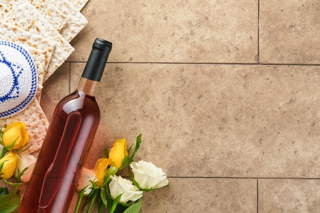 Passover celebration concept Matzah kosher red wine walnut and white and yellow roses Traditional ritual Jewish bread on sand color old tile wall background Passover food Pesach Jewish holiday