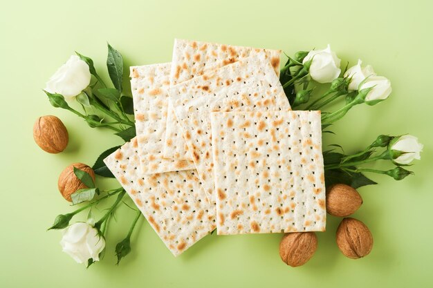 Passover celebration concept Matzah red kosher wine walnut and spring beautiful rose flowers Traditional ritual Jewish bread on light green background Passover food Pesach Jewish holiday