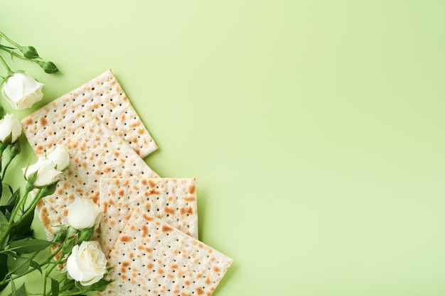 Passover celebration concept Matzah red kosher wine walnut and spring beautiful rose flowers Traditional ritual Jewish bread on light green background Passover food Pesach Jewish holiday