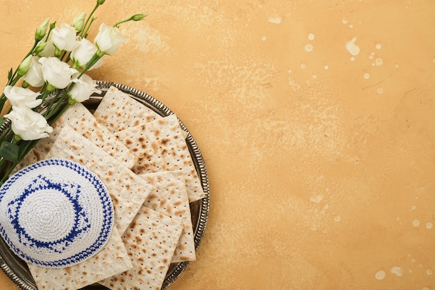 Passover Pesah celebration concept Matzah kosher red wine walnut and white and yellow roses Traditional ritual Jewish bread on sand color old tile wall background Pesach Jewish holiday Top view