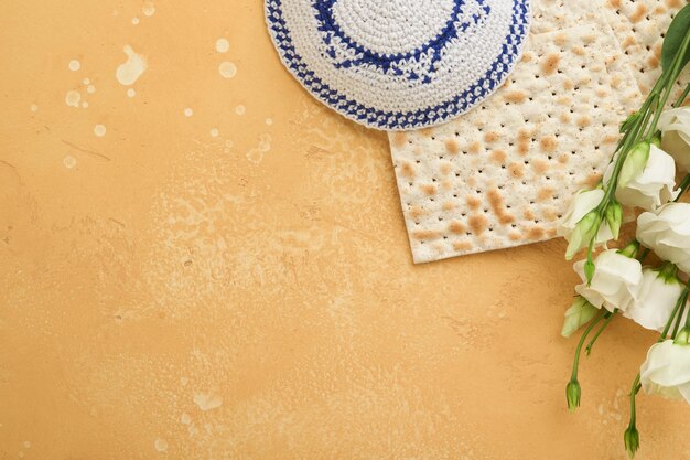 Passover Pesah celebration concept Matzah kosher red wine walnut and white and yellow roses Traditional ritual Jewish bread on sand color old tile wall background Pesach Jewish holiday Top view