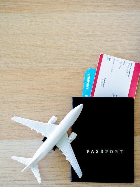 Черная обложка паспорта с билетом на самолет рядом с белой игрушкой самолета на деревянном столе с копировальным пространством, вид сверху в вертикальном стиле Онлайн-бронирование билетов для концепции путешествия
