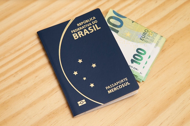 Passport with 100 euro banknotes on the side, on wooden table.