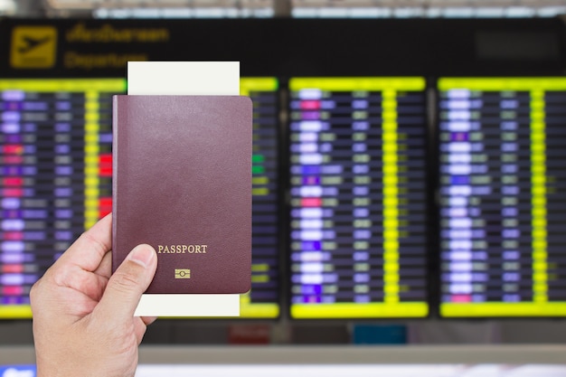 写真 ぼやけたフライト出発情報表示画面で男性の手に搭乗券があるパスポート