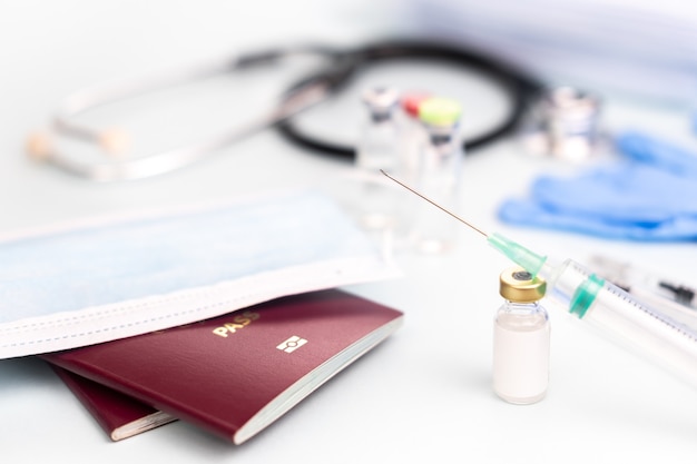 Passports with medical mask with ampoule mock-up for vaccination with syringe on blurred