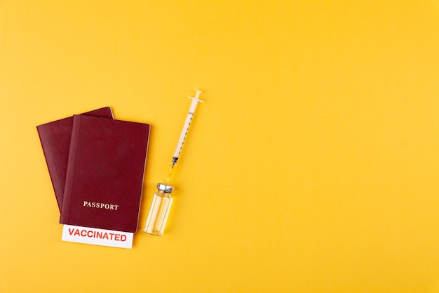 Passports with vaccinated stamp on blank syringe bottle with vaccine on yellow background