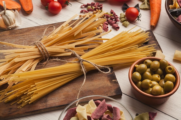 Pasta achtergrond. Fettuccine, spaghetti, groenten en kruiden op witte houten achtergrond. Diverse Italiaanse macaroni en kookingrediënten