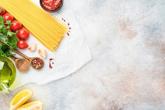 Pasta background. Pasta spaghetti, tomato ketchup sauce, olive oil, spices, parsley, and fresh tomatoes on a light grey slate table. Food cooking background. Top view with copy space.