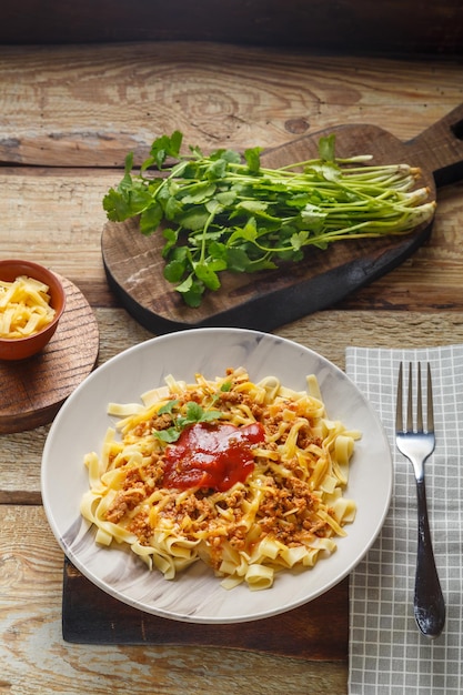 Pasta bolognese garnished with greens and cheese in a plate on a wooden table on a glossy
