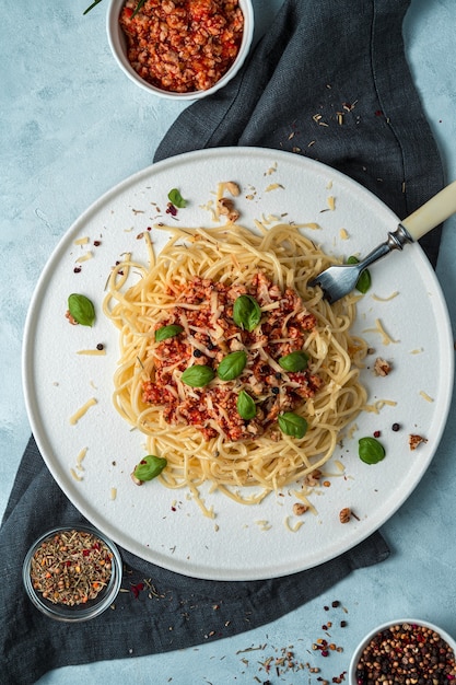 Pasta bolognese with basil and nuts in a flat plate on a dark napkin on a gray background.