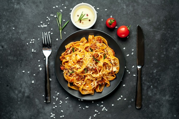 Pasta alla bolognese con spezie, piatto di pasta italiana con carne macinata e pomodori in un piatto scuro su uno sfondo di pietra