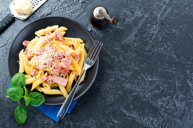 Pasta carbonara met prosciutto en parmezaanse kaas op zwarte tafel. Bovenaanzicht.