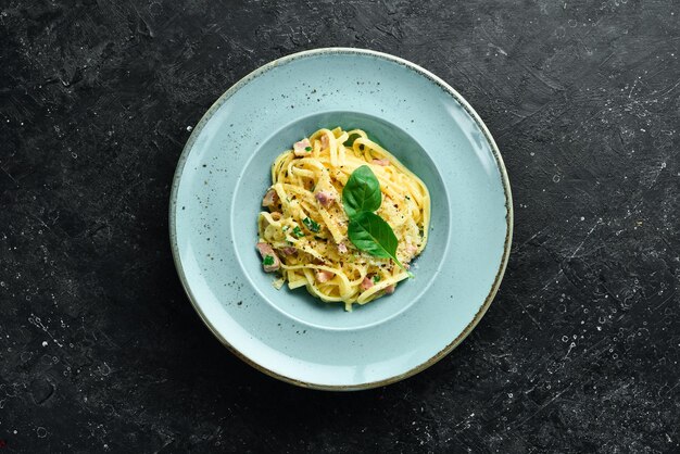 Pasta carbonara met spek, kaas en basilicum in een bord Italiaanse schotel op een zwarte stenen achtergrond