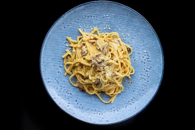 Pasta carbonara with bacon on blue plate isolated on black background top view