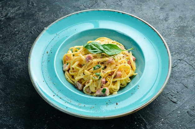 Pasta carbonara with bacon cheese and basil in a plate Italian dish On a black stone background