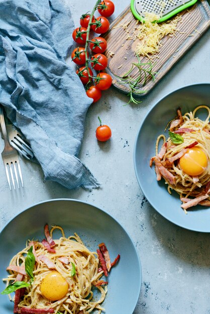 Pasta carbonara with bacon and parmesan in gray plates on the\
table, restaurant serve on a blue wall. traditional italian\
cuisine. home family dinner.view from above