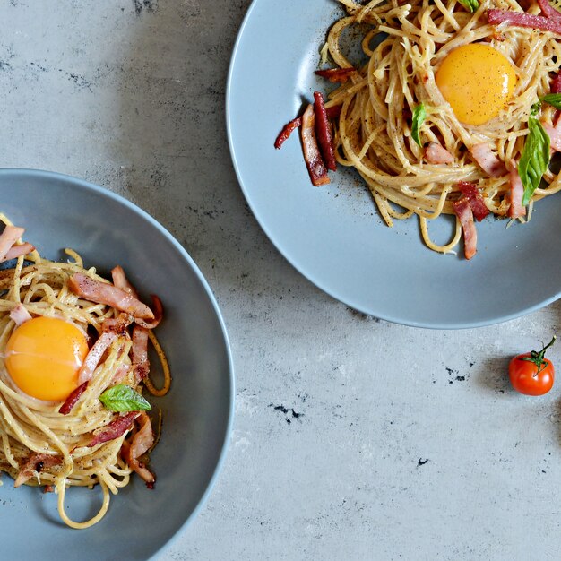 Pasta carbonara with bacon and parmesan in gray plates on the table, restaurant serve.