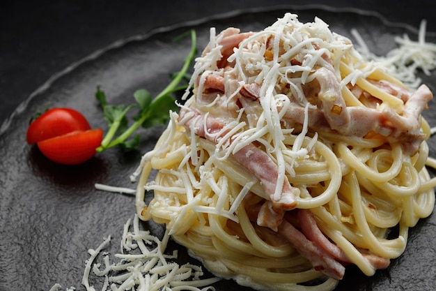 Pasta Carbonara with tomatoes on a black plate on a black background