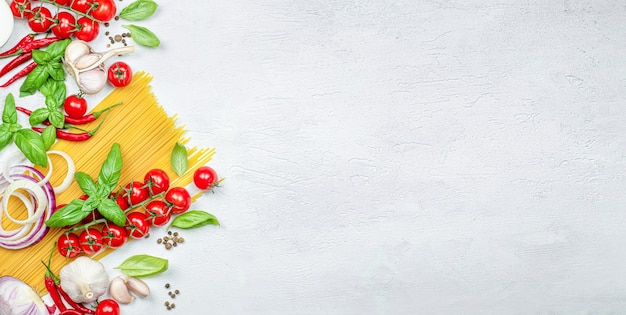 Pasta, cherry tomato, onion, garlic, peppercorns, chili peppers and basil on a gray table