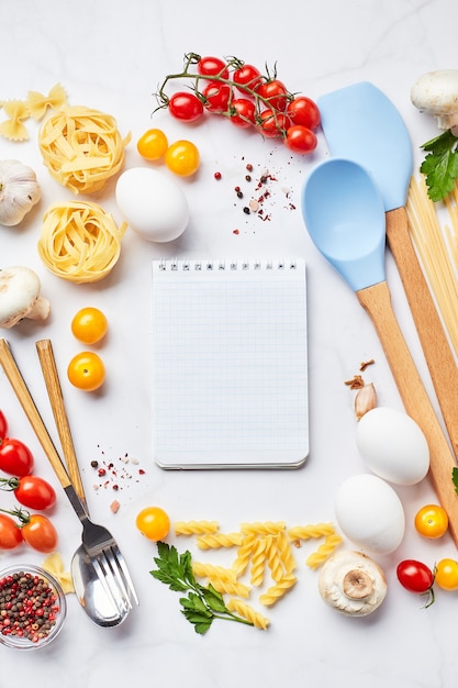 Foto pasta che cucina sfondo con blocco note per testo, pomodori, erbe aromatiche, funghi, uova sparse su sfondo di marmo chiaro, vista dall'alto. concetto di cucina italiana