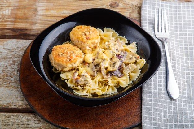 Pasta in a creamy sauce with mushrooms and chicken meatballs in a black plate on a napkin next to a fork. Horizontal photo