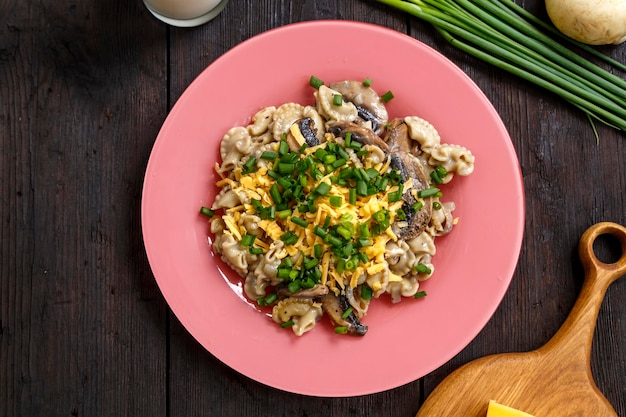 Pasta in a creamy sauce with mushrooms in a plate on the table next to green onion feathers and cheese