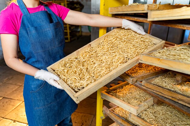 Pasta fabriek. Productie van deegwaren. Gekrafte macaroni. Werknemer met houten kist met pasta.