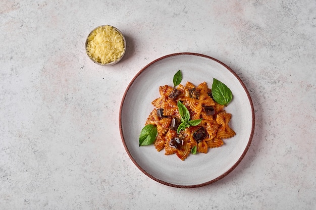 Pasta farfalle met aubergine tomatensaus kaas in kom en basilicum op plaat op een grijze textuur