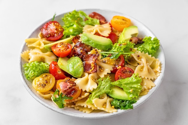Photo pasta farfalle salad with tomato bacon avocado and mustard dressing in a plate on white table close up