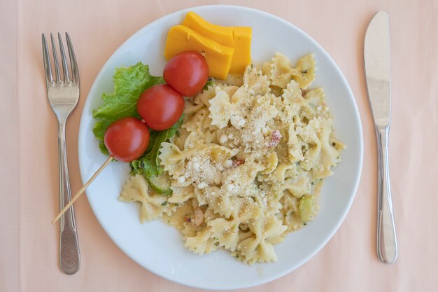 Farfalle di pasta con pomodorini e formaggio in piatto bianco, primo piano