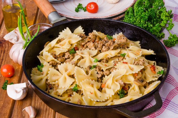 Pasta farfalle with fried meat, mushrooms and vegetables. Rustic style.