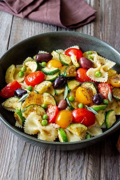 Farfalle di pasta con pomodori zucchine piselli olive kalamata e salvia alimentazione sana cibo vegetariano