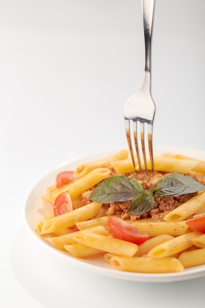 Fettuccine alla bolognese con salsa al pomodoro e basilico in piatto bianco su bianco