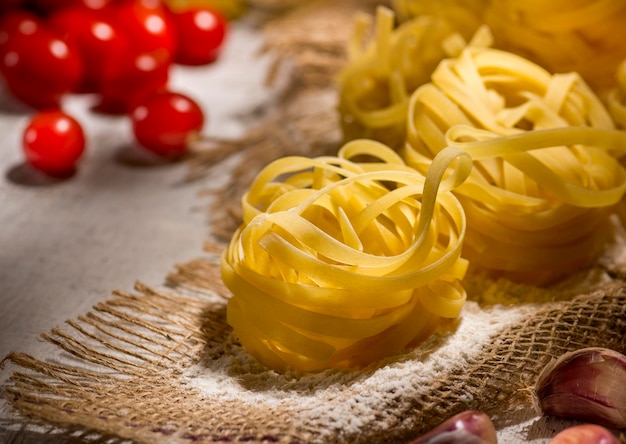 Pasta fettuccine on wooden table with cherry tomatoes and eggs in background.