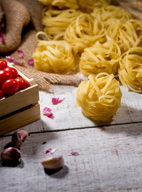 Pasta fettuccine on wooden table with cherry tomatoes and garics in background, space for text.