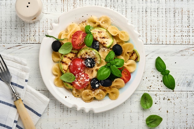 Pasta fiocchi salad with vegetables grilled zucchini, cherry tomato, olives, basil and parmesan cheese in white plate on light slate, stone or concrete background. Lunch concept. Top view.