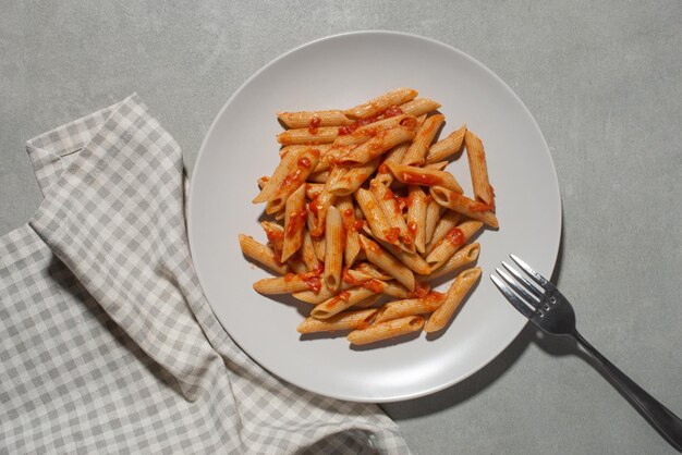 Pasta on a fork with tomatoes and cheese in a plate on a gray background