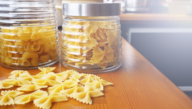 Foto pasta sotto forma di fiocchi sparsi dal barattolo di vetro. pasta fatta a mano italiana sui precedenti di legno.