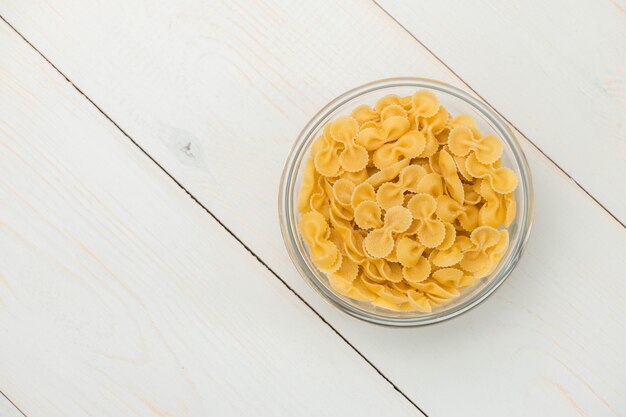 Pasta in the form of glass butterflies in a transparent bowl on a white old wooden boards