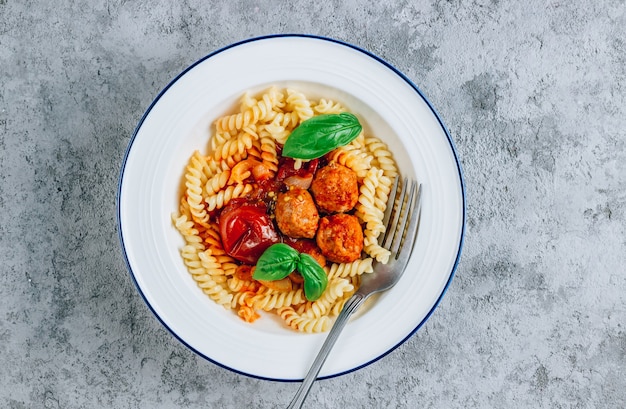 Fusili di pasta con polpette, pomodoro e basilico in due ciotole su fondo in cemento