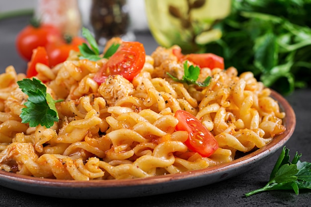 Pasta Fusilli met tomaten, kippenvlees en peterselie op plaat op donkere tafel.