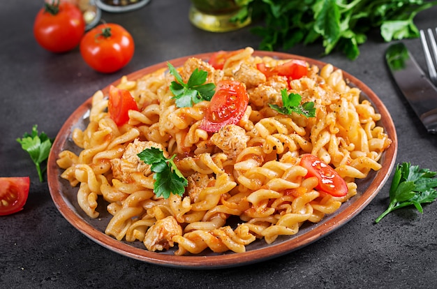 Pasta Fusilli met tomaten, kippenvlees en peterselie op plaat op donkere tafel.