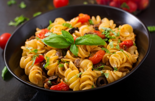 Pasta Fusilli met tomaten, rundvlees en basilicum in zwarte kom op tafel.