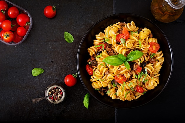 Pasta Fusilli  with tomatoes, beef and basil in black bowl on table. Top view. Flat lay