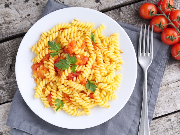 Pasta fusilli with tomatoes with parsley on a old rustic table, low-calorie diet, top view.