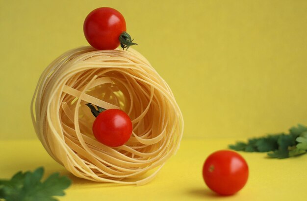 Pasta in de vorm van een nest met tomaten en peterselie op een gele achtergrondbalans van producten