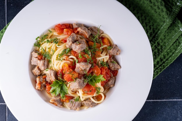 Pasta in tomatensaus en vlees op witte plaat en zwarte keramische achtergrond. bovenaanzicht.