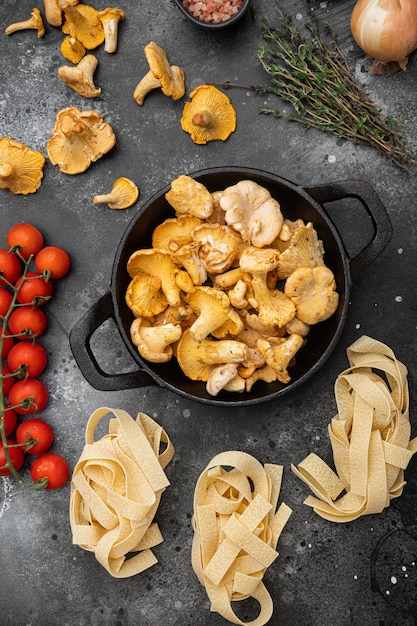 Pasta-ingrediënten met rauwe paddenstoelen, cantharellen, op een zwarte rustieke tafelachtergrond, bovenaanzicht plat gelegd