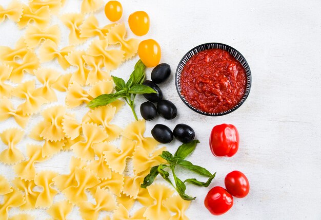 Pasta ingredients, raw pasta, cherry tomatoes, olives and basil leaves on the white background